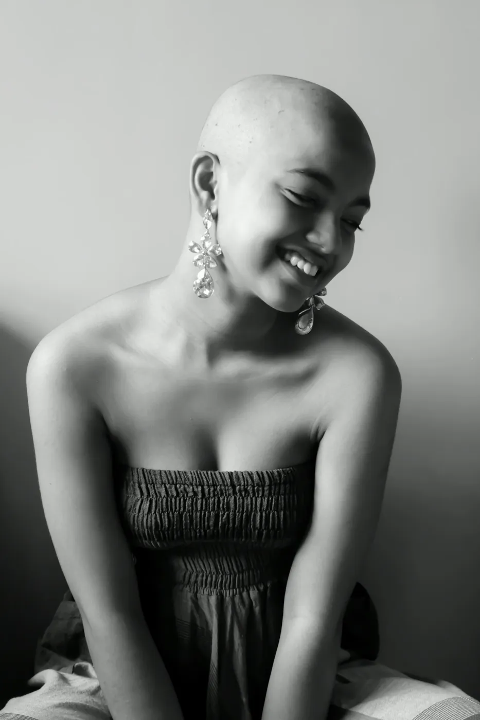 A woman with a shaved head smiles, wearing long statement earrings