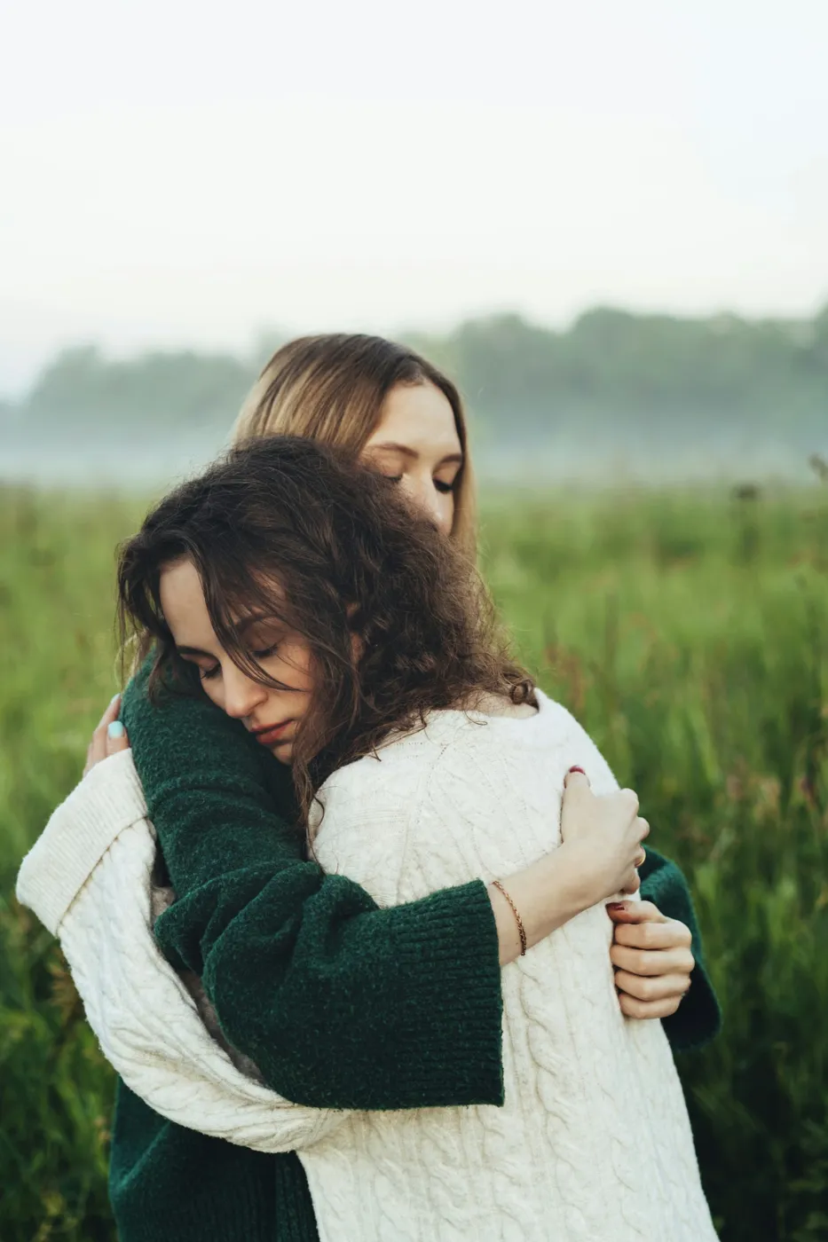 Two women hold each other in a long embrace in a field
