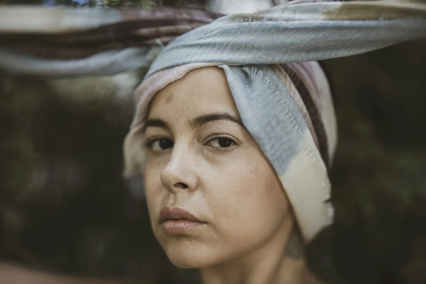 A woman in a soft head wrap looks calmly toward the camera